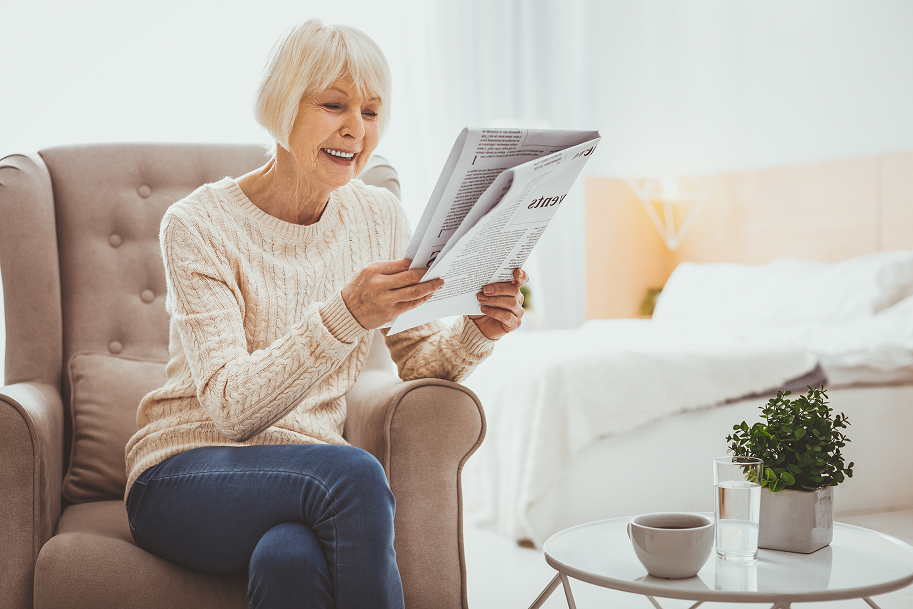 Aeltere Frau sitzt nachdenklich mit Buch im Wohnzimmer - Symbolbild fuer unsichtbare Beschwerden bei Polyneuropathie